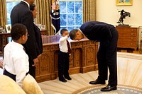President Barack Obama bends over so the son of a White House staff member can pat his head during a family visit to the Oval Office May 8, 2009.