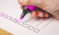 Side view of a hand writing on a checklist with magenta marker on the wooden surface