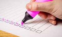 Side view of a hand writing on a checklist with magenta marker on the wooden surface