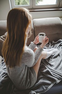 Free woman sits on the sofa drinking coffee photo, public domain CC0 image.