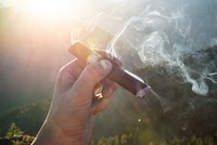 Hand of a smoking man holding a burning cigar with mountains in the background