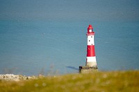 Red and white lighthouse on cliff by seashore. Free public domain CC0 photo.