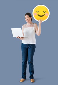 Woman holding a blushing emoticon and a laptop