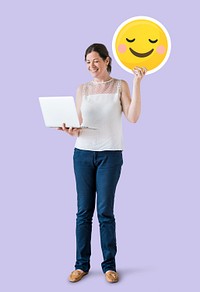 Woman holding a blushing emoticon and a laptop