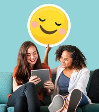 Women holding a blushing emoticon and using a tablet