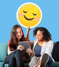 Women holding a blushing emoticon and using a tablet