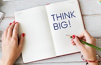 Woman writing Think big on a notebook