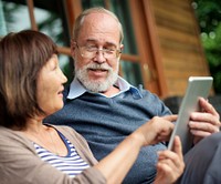 Senior couple sitting in front of a wooden cabin sharing a tablet