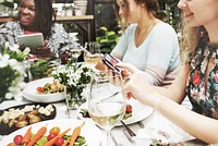 Group of diverse women having meal together using digital devices