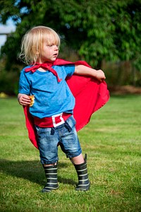 Little boy wearing superhero costume playing in a park