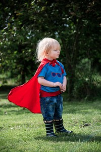 Little boy wearing superhero costume playing in a park