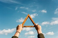 Hands holding wooden triangle frame up in a blue sky
