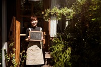 Welcoming woman holding an open sign in front of a cafe shop<br />