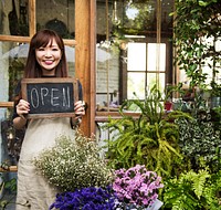 Welcoming florist holding an open sign in front of a flower shop<br />