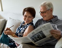 Senior couple in a living room reading a newspaper and knitting