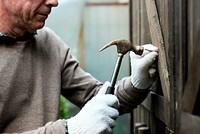 Elderly man fixing a wooden door with hammer