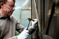 Elderly man fixing a wooden door with hammer