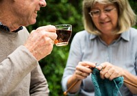 Old couple enjoying tea and knitting outdoors
