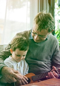 Grandfather teaching little cute grandson to play ukulele