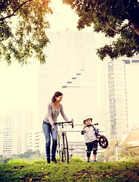 Little boy and his mother riding bicycle in the park with cityscape background