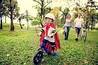 Superhero little boy riding bicycle with family in the park