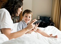 Mother and son playing on smartphone in bed