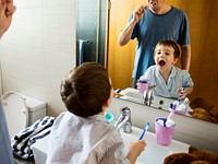 Father teaching the son how to brush his teeth