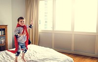 Playful superhero little boy jumping on the bed