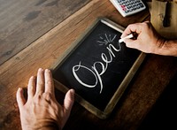 Closeup of hands writing open word on chalkboard