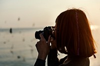 Girl taking photos of birds flying above the ocean