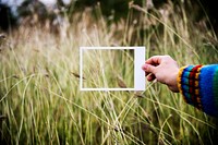 Hand holding a photo frame border to the grass field
