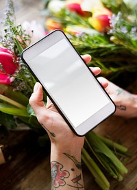 Tattooed hands with mobile phone with blank screen and bouquet of flowers