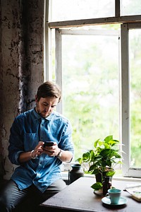Caucasian guy using mobile phone sitting by the window