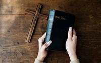 Hands Holding Holy Bible Next to Wooden Cross
