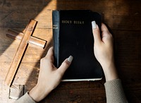 Hands Holding Holy Bible with Wooden Cross
