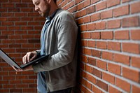 Man lean on brick wall and using laptop