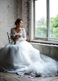 Bride in her gown with a bouquet of flowers sitting by the window