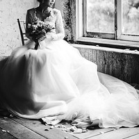 Bride in her gown with a bouquet of flowers sitting by the window