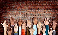 Group of Diverse Hands Raised on Brick Wall