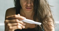 Woman holding pregnancy test with depressed worried face expression