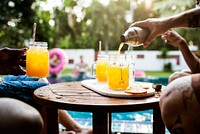 Hand pouring orange beverage to glasses by the pool