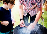 Closeup of father preparing charcoal grill for barbecue party with son