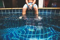 Young caucasian boy put feet in swimming pool