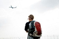 Young caucasian traveler standing outdoors with a takeoff airplane