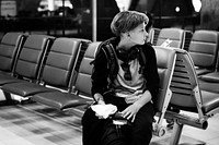 Young caucasian man sitting waiting at airport grayscale