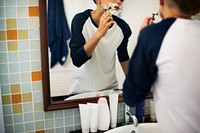 Young caucasian man shaving beard in bathroom