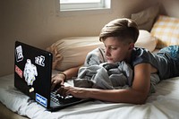 Young caucasian boy lying using computer laptop on bed