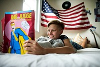 Young caucasian boy lying reading cartoon on bed