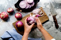 Aerial view of hands with knife cutting red onion on cut board