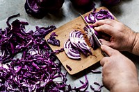 Closeup of hands with knife cutting red cabbage on cut board